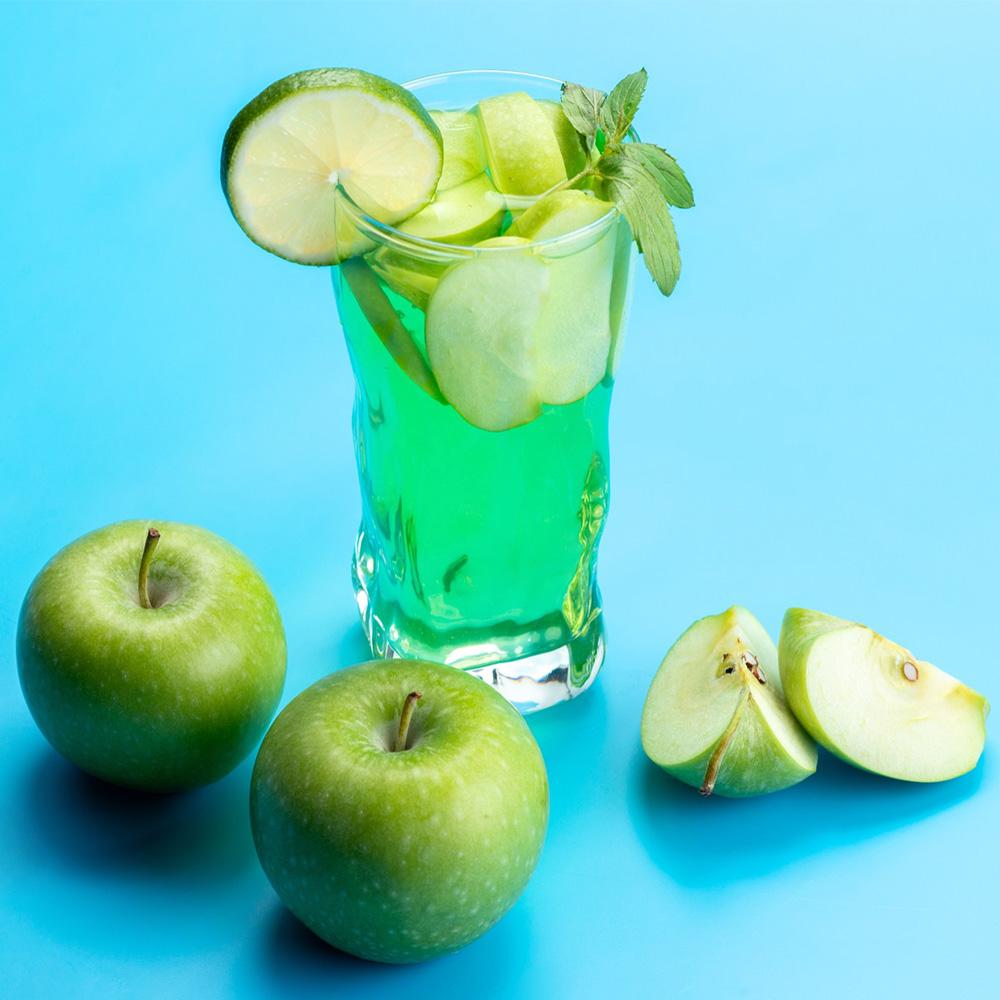 Troisième photo du slider pour la page verger d'un cocktail de fruits avec des pommes vertes présentées autour du verre et deux cartiers de pommes sur un fond bleu clair