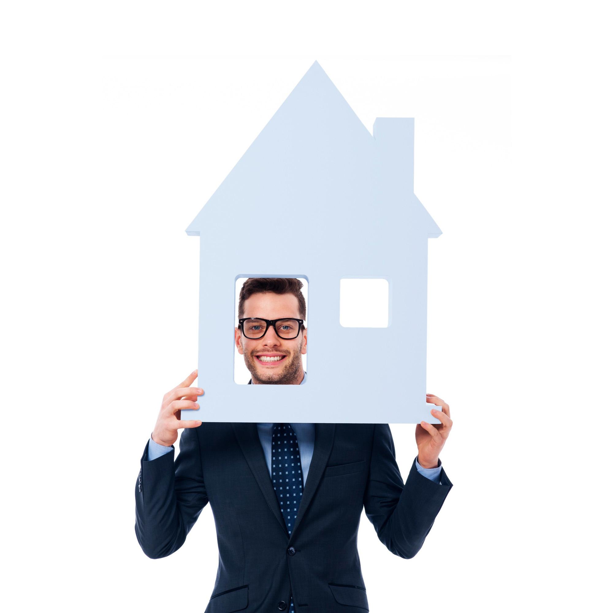 Photo d'un homme  tenant une maison en carton blanc qui regarde par la porte pour le visuel de la page de couverture rubrique agence immobilière.